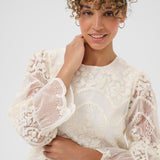 Woman wearing a white lace top against a plain background