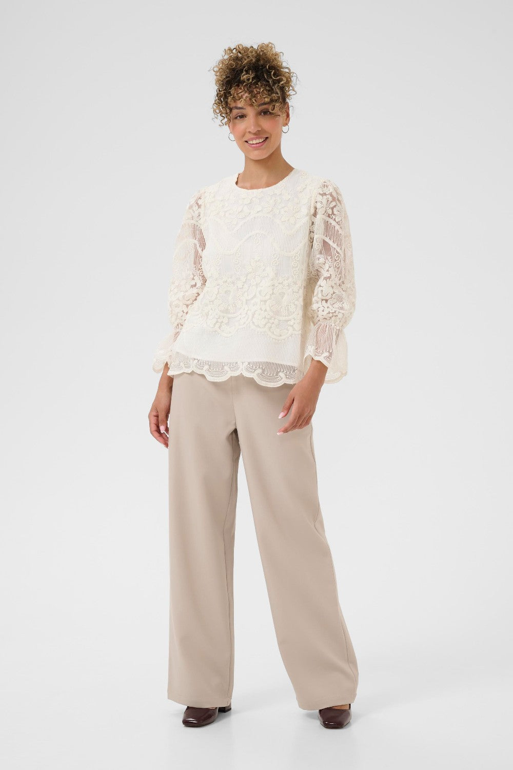 Woman wearing a white lace top and beige pants on a white background