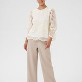 Woman wearing a white lace top and beige pants on a white background