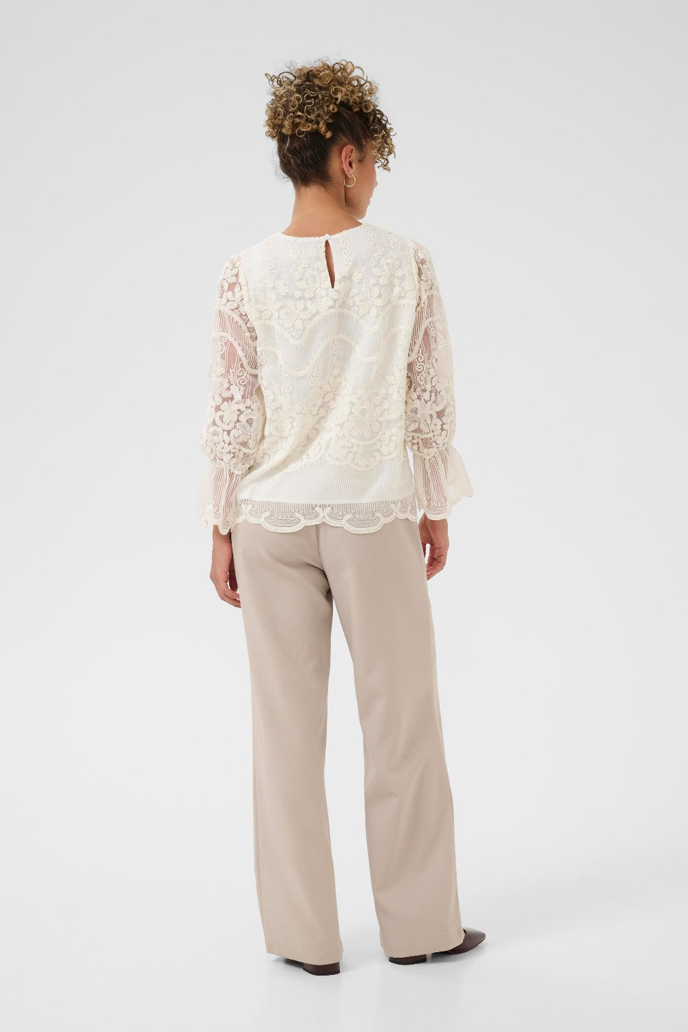 Person wearing a white lace top and beige pants on a white background