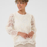 Woman wearing a white lace top with a plain background