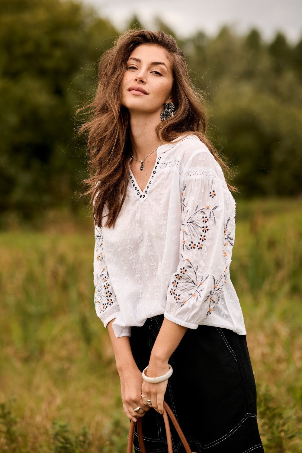 Woman in a white blouse with floral embroidery standing in a field.