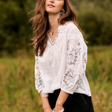 Woman in a white blouse with floral embroidery standing in a field.