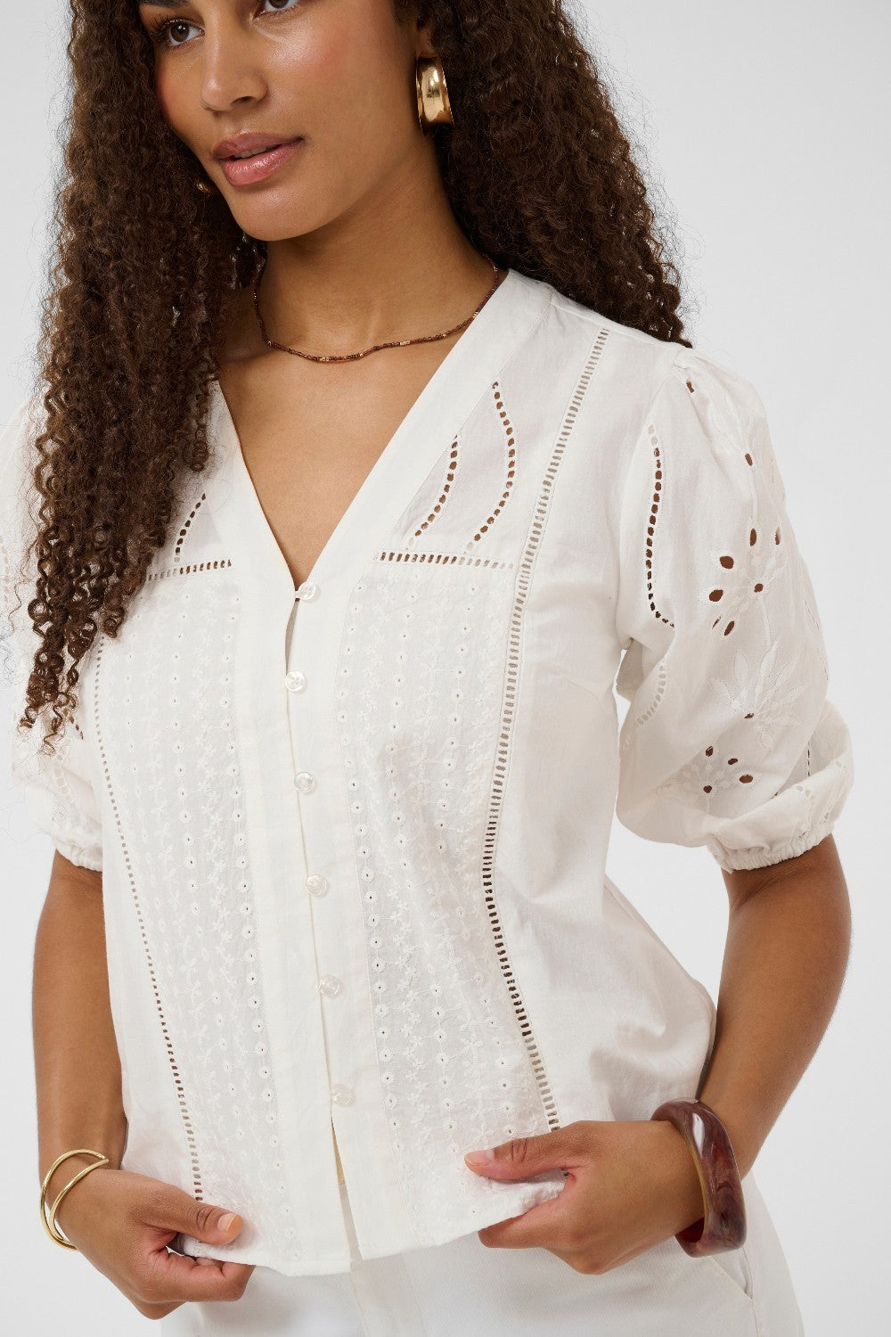 Woman wearing a white embroidered blouse against a plain background