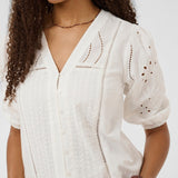 Woman wearing a white embroidered blouse against a plain background