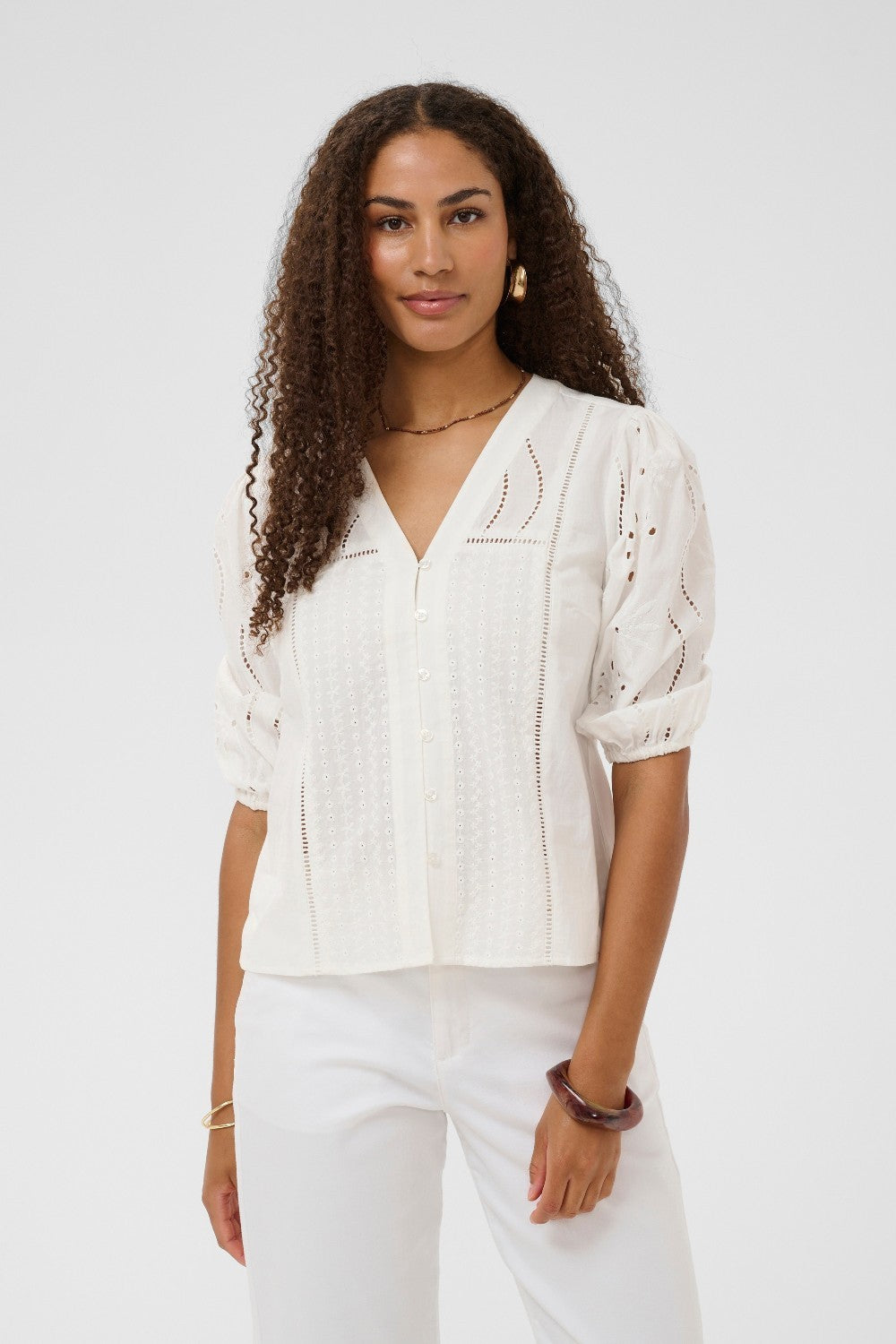 Woman wearing a white blouse with intricate patterns on a plain background
