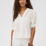 Woman wearing a white blouse with intricate patterns on a plain background