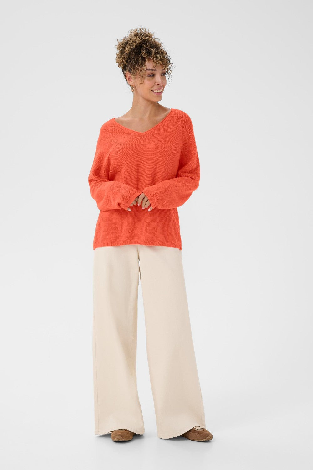 Woman wearing an orange sweater and beige pants on a white background