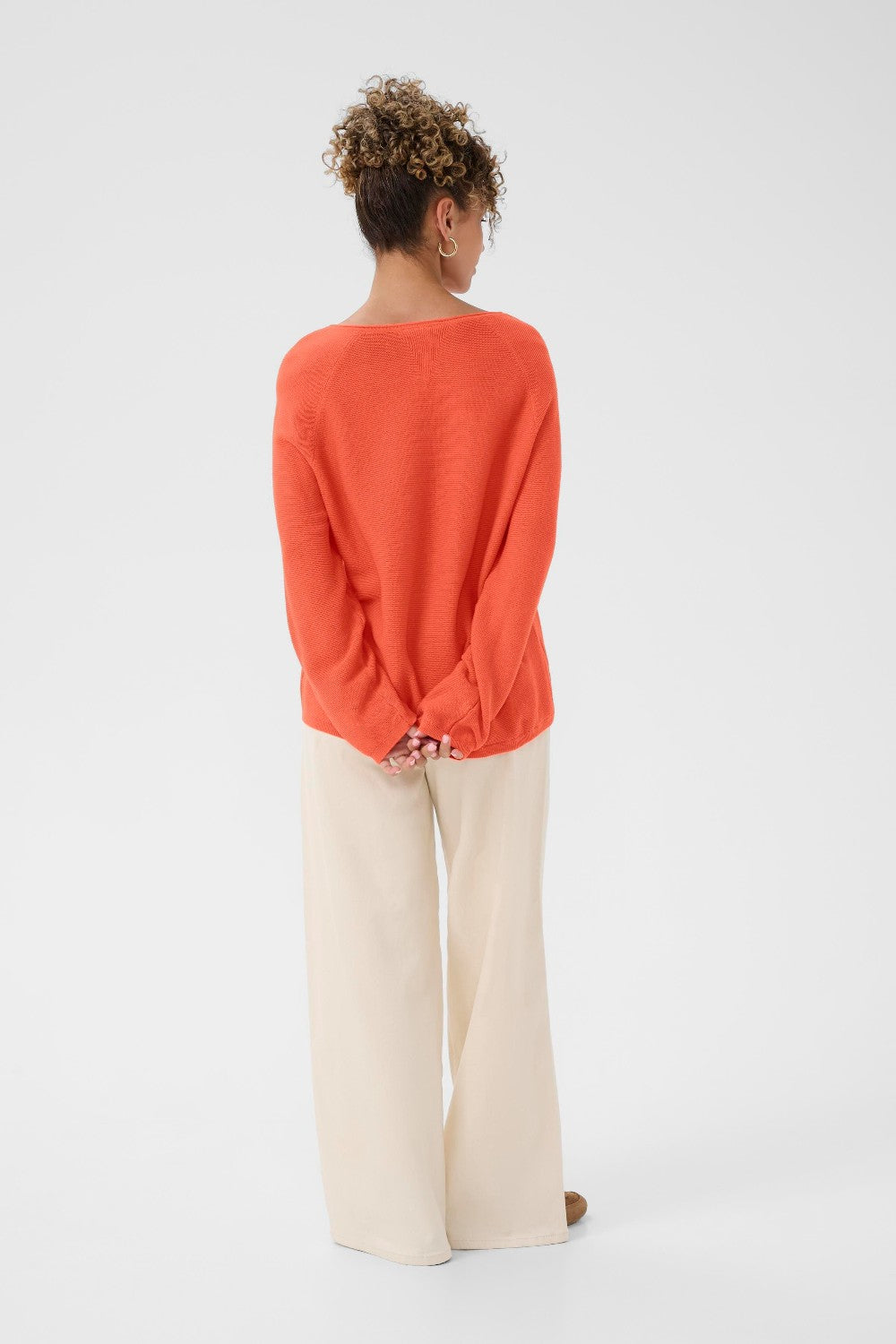 Person wearing an orange sweater and beige pants on a white background