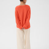 Person wearing an orange sweater and beige pants on a white background