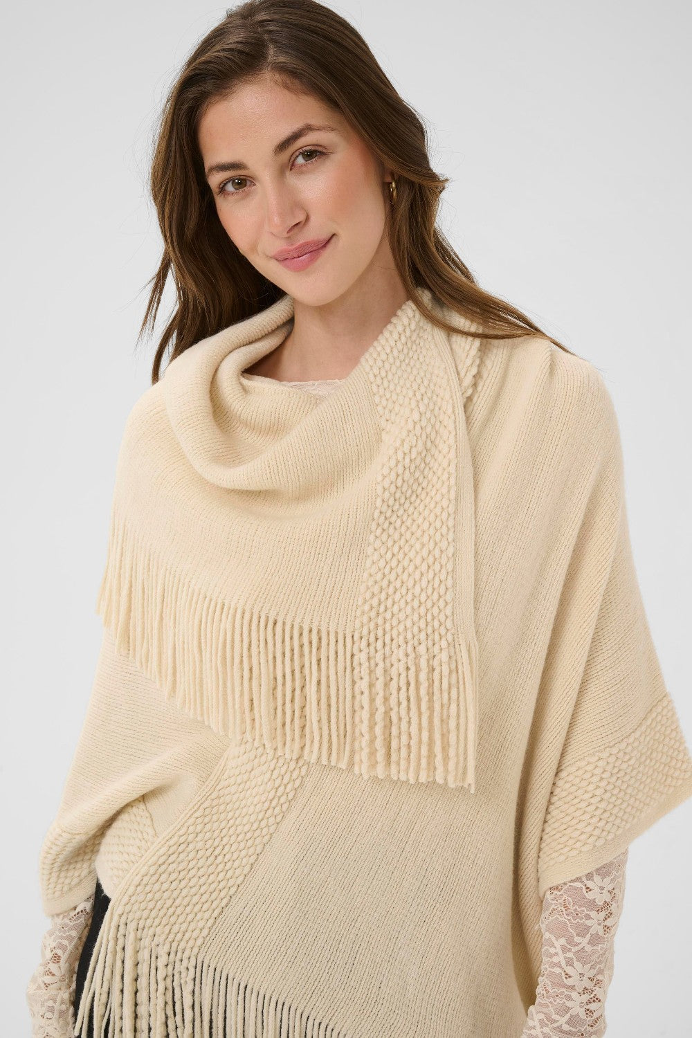 Woman wearing a beige poncho with fringe details on a white background
