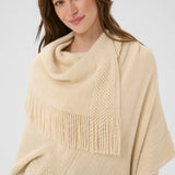 Woman wearing a beige poncho with fringe details on a white background