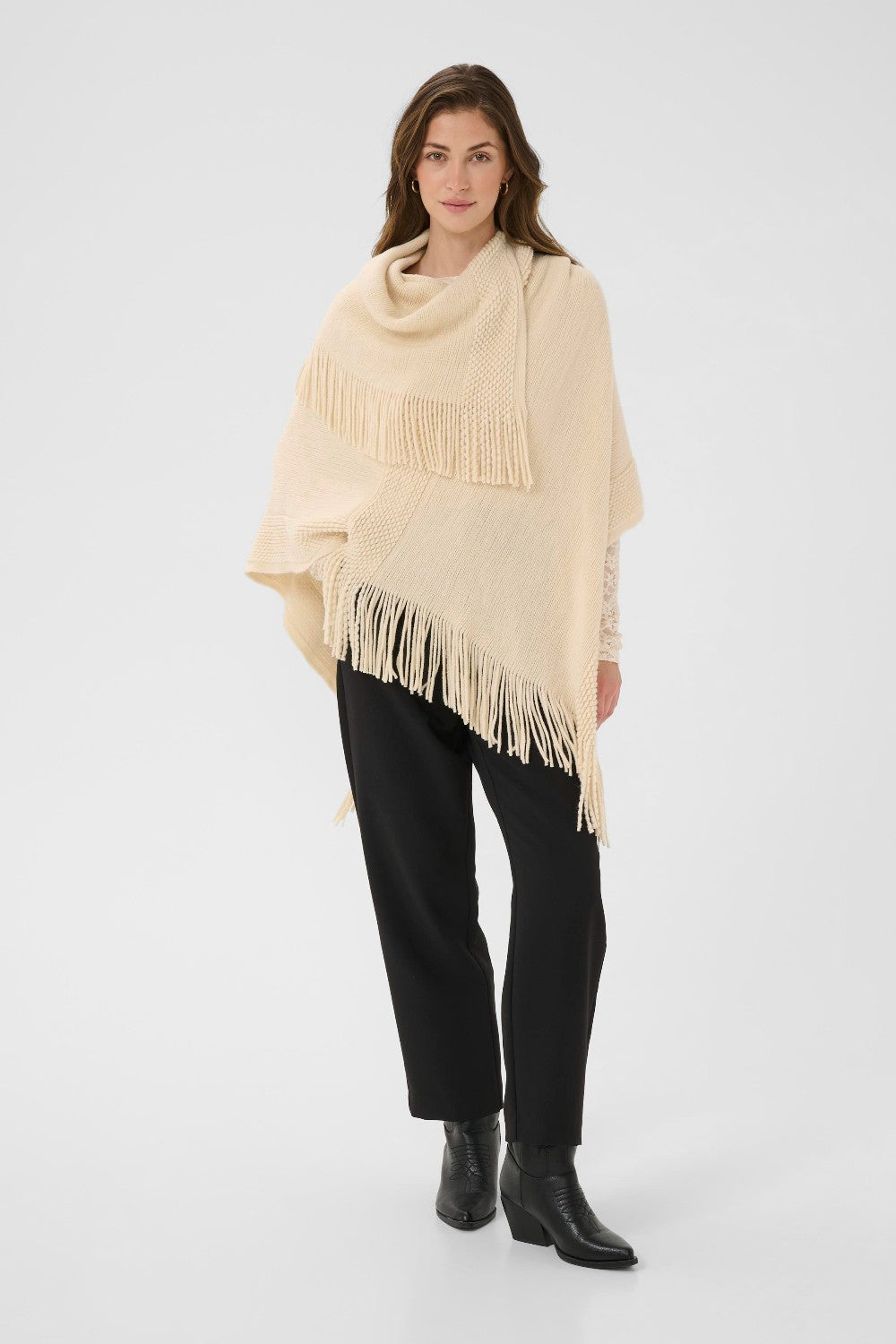 Woman wearing a beige poncho with fringe on a white background