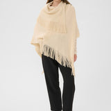 Woman wearing a beige poncho with fringe on a white background