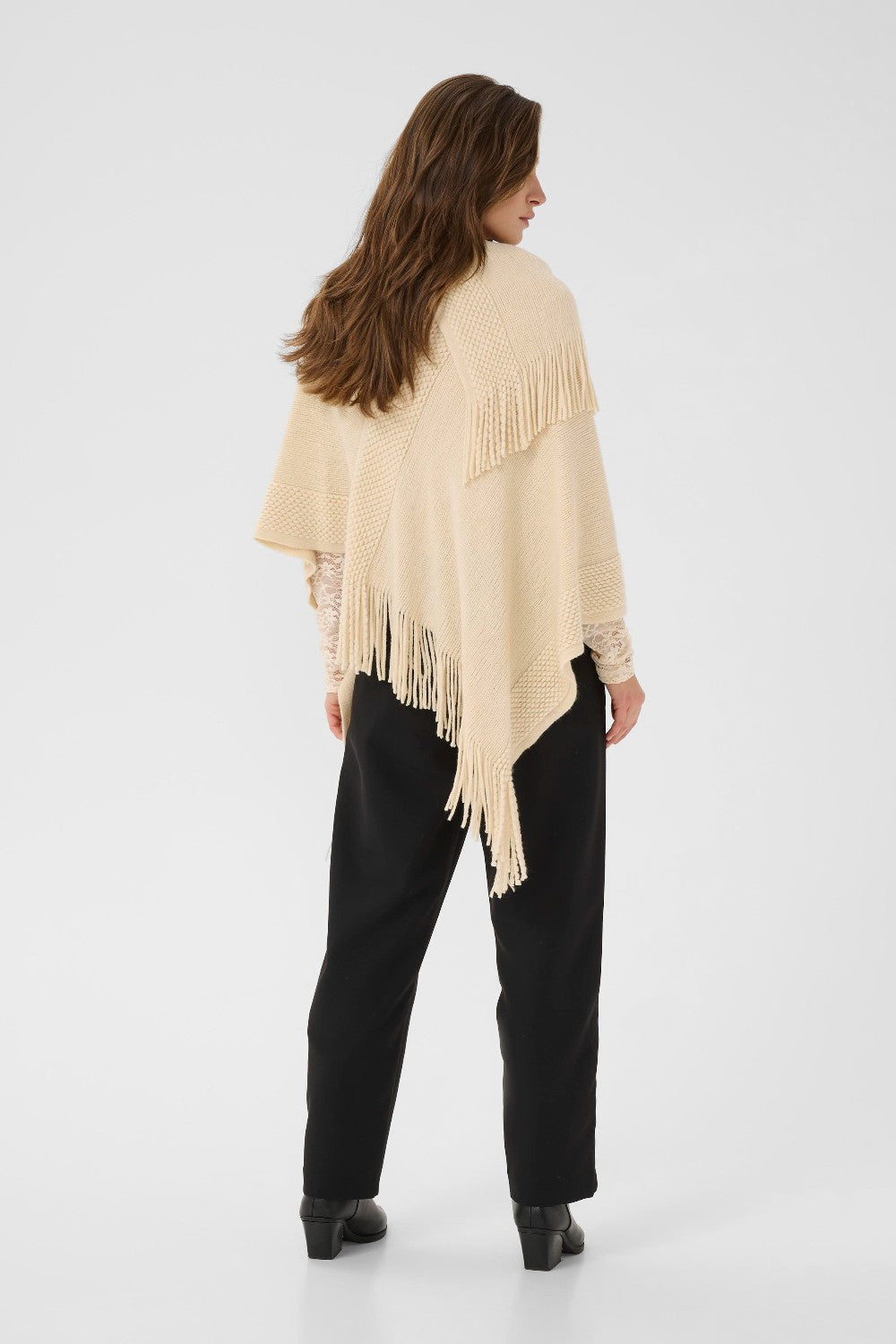 Woman wearing a beige fringe poncho on a white background