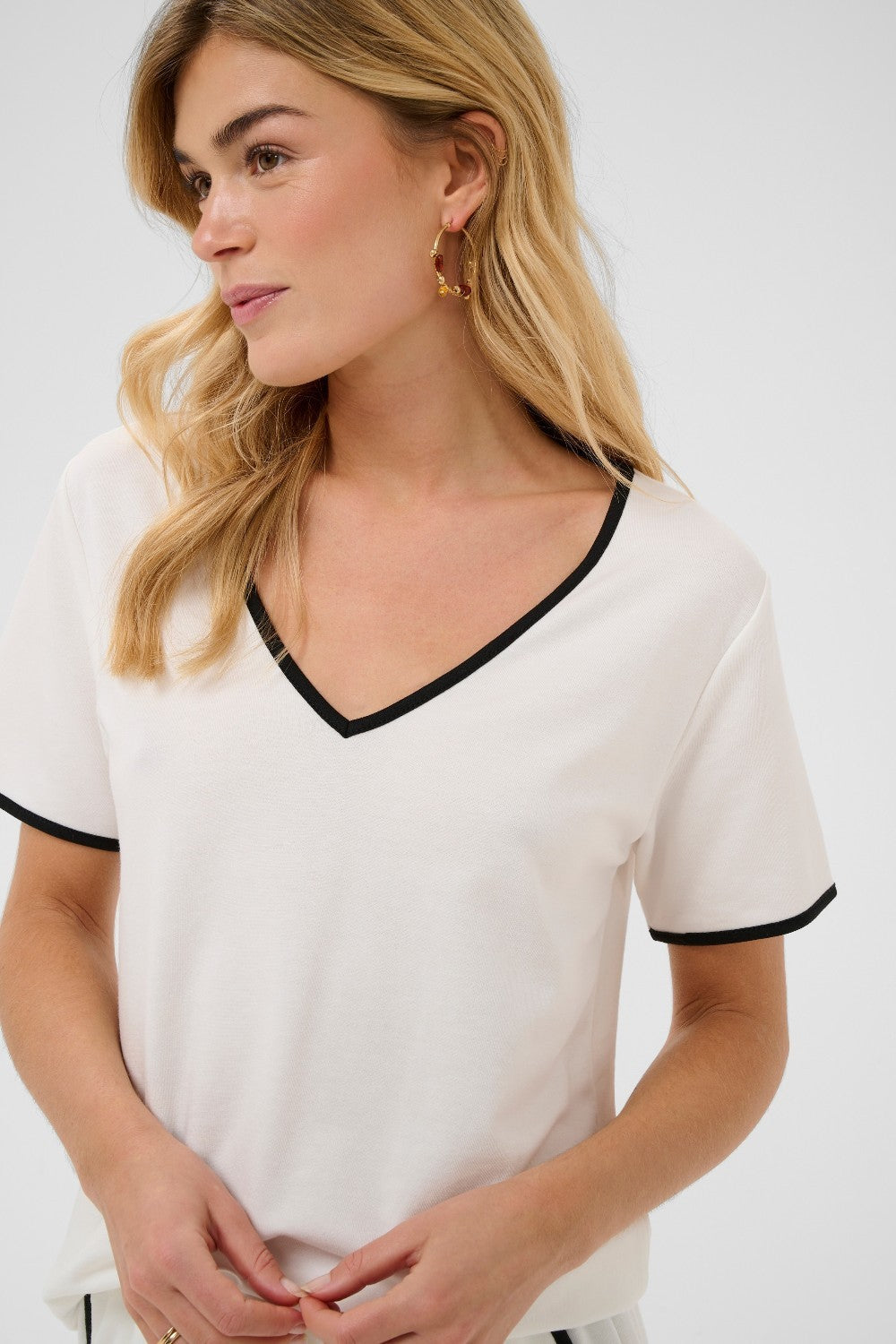 Woman wearing a white top with black trim on a plain background