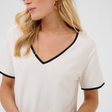 Woman wearing a white top with black trim on a plain background