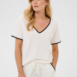 Woman wearing a white outfit with black trim on a plain background
