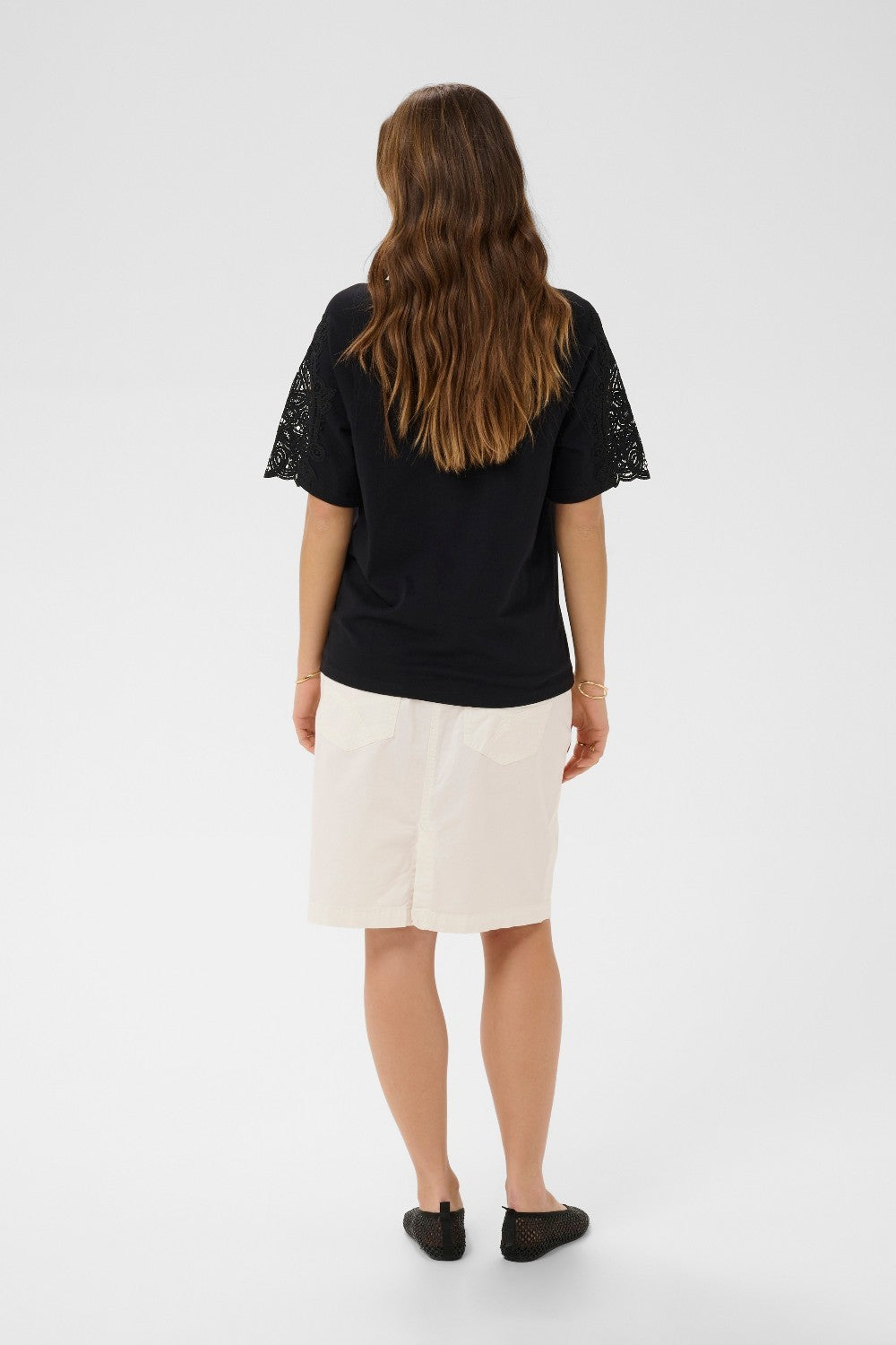 Woman wearing a black top with lace sleeves and a white skirt on a white background