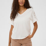 Woman wearing a white top with lace sleeves on a plain background