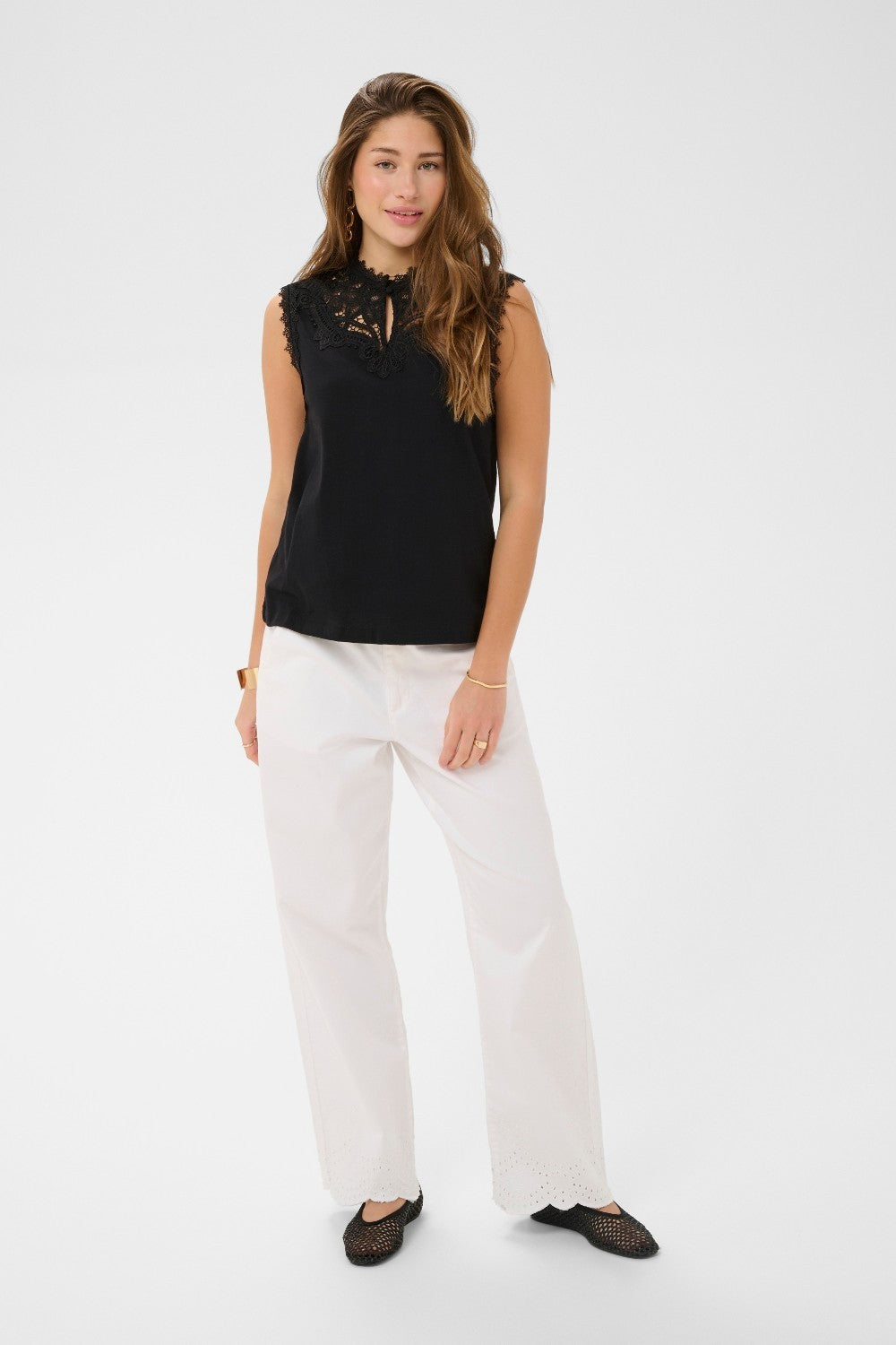 Woman wearing a black sleeveless top and white pants on a white background