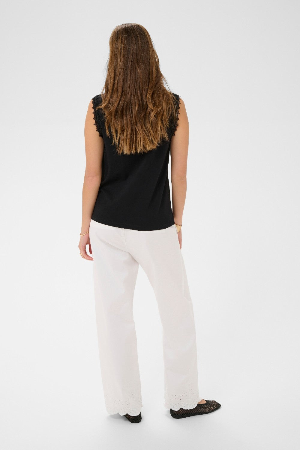 Person wearing a black sleeveless top and white pants on a white background