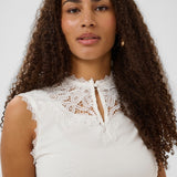 Woman wearing a white lace top against a plain background