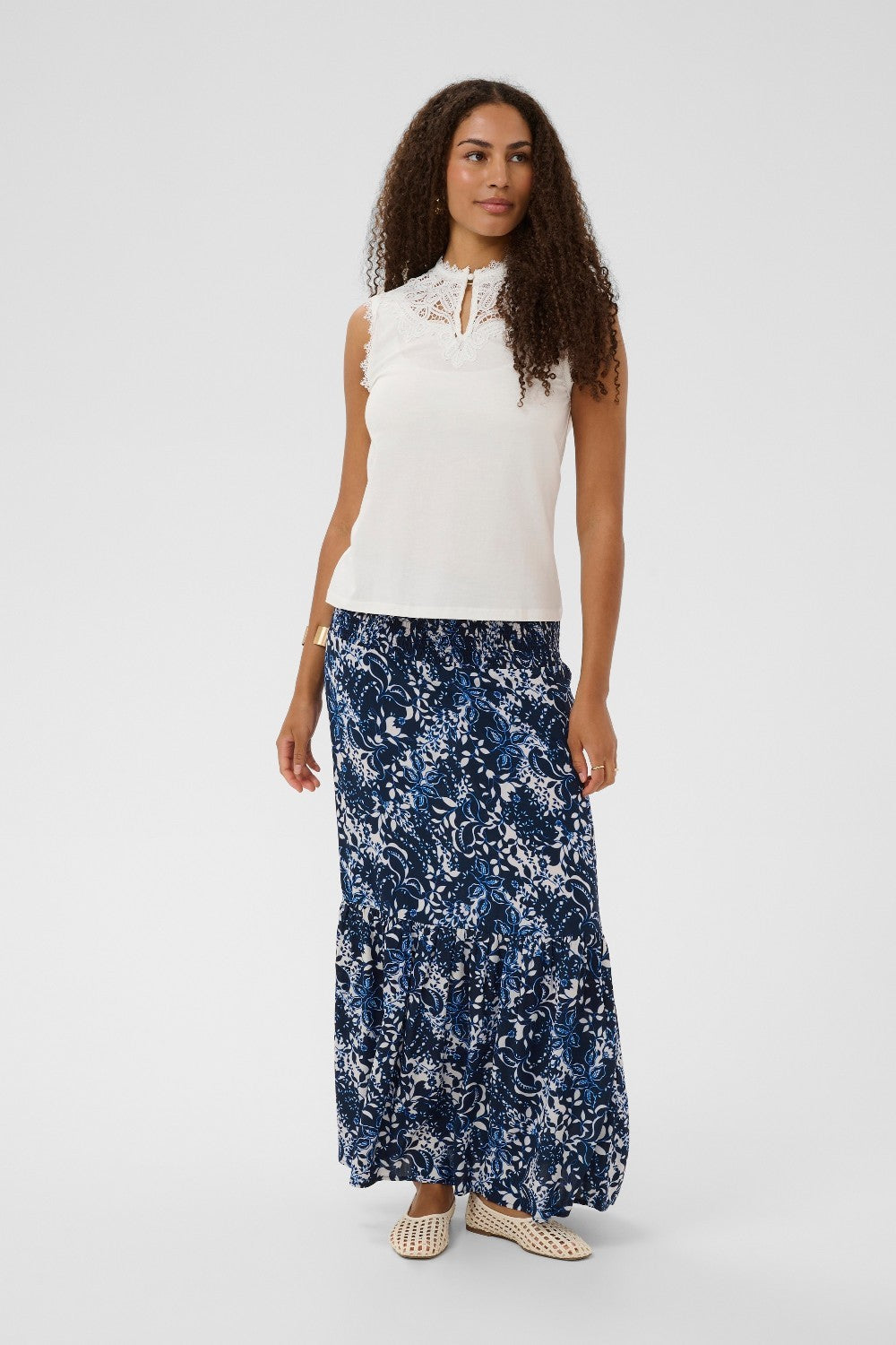 Woman wearing a white sleeveless top and blue floral maxi skirt on a white background