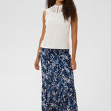 Woman wearing a white sleeveless top and blue floral maxi skirt on a white background
