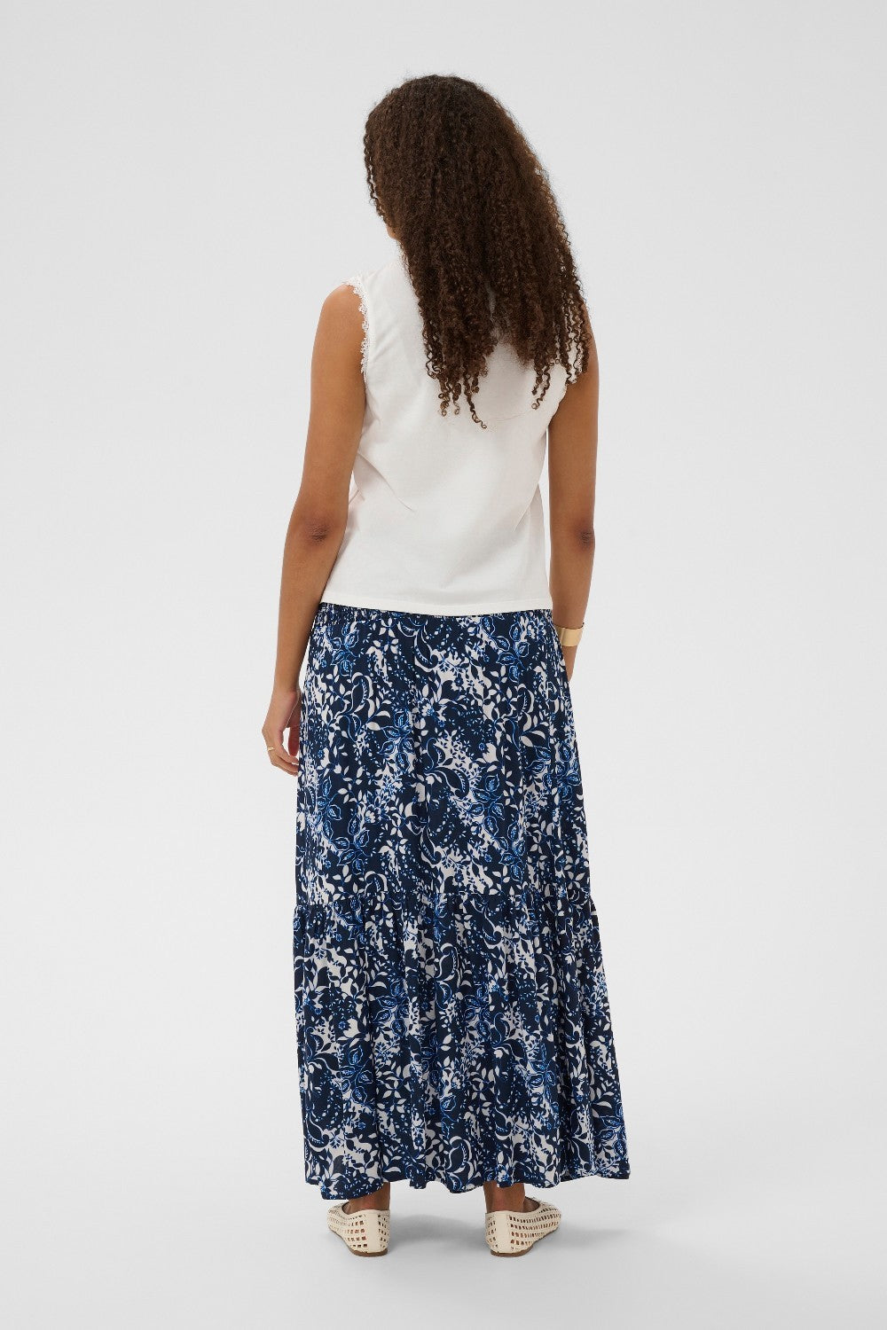 Woman wearing a white sleeveless top and blue floral skirt on a white background