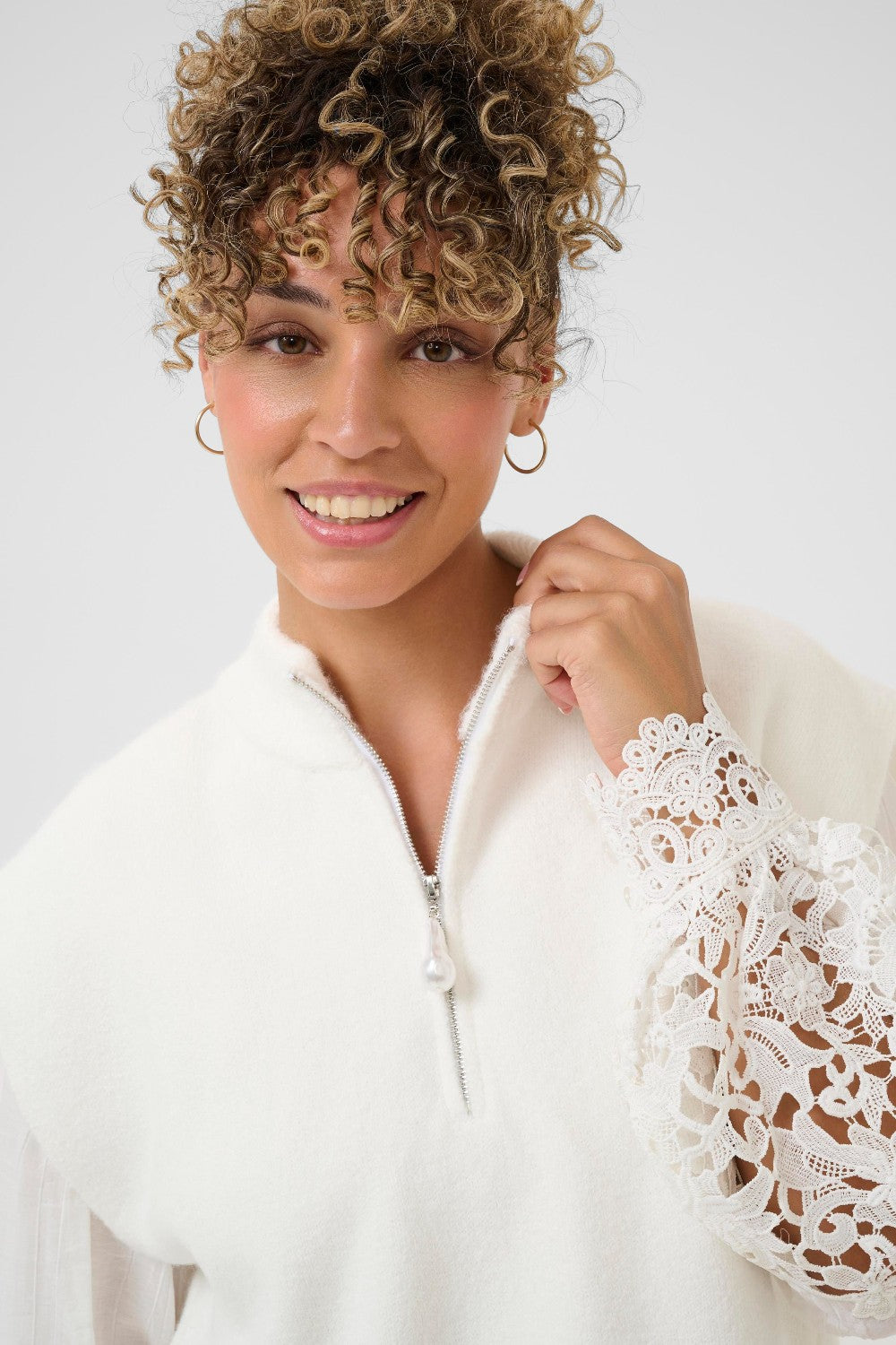 Woman wearing a white vest and blouse with lace sleeves against a plain background