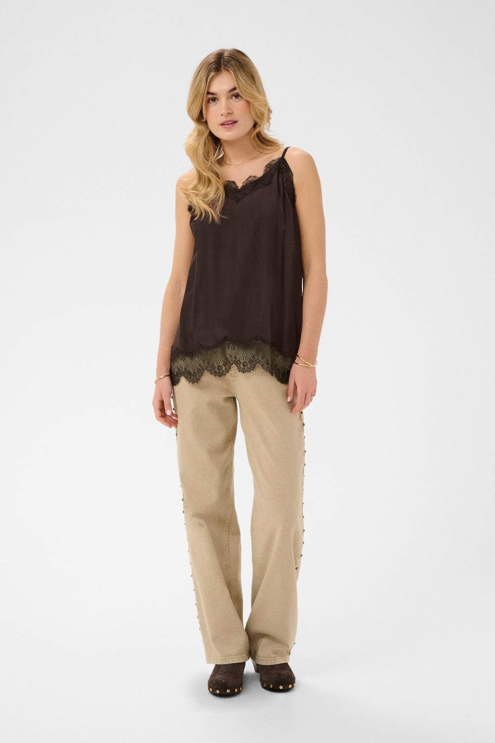 Woman wearing a brown sleeveless top with lace details and beige pants on a white background