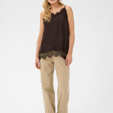 Woman wearing a brown sleeveless top with lace details and beige pants on a white background