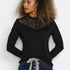 Woman wearing a black long-sleeve top with lace detailing and blue jeans against a white background