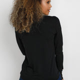 Woman wearing a black long-sleeve top and blue jeans against a white background