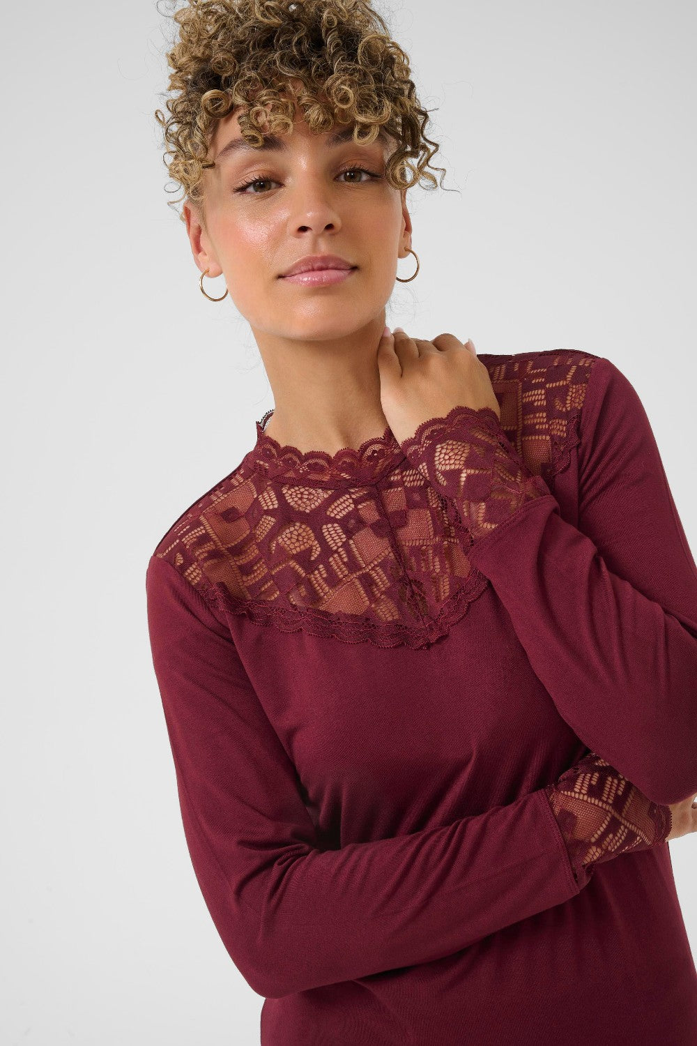 Woman wearing a burgundy top with lace details on a white background