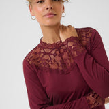 Woman wearing a burgundy top with lace details on a white background