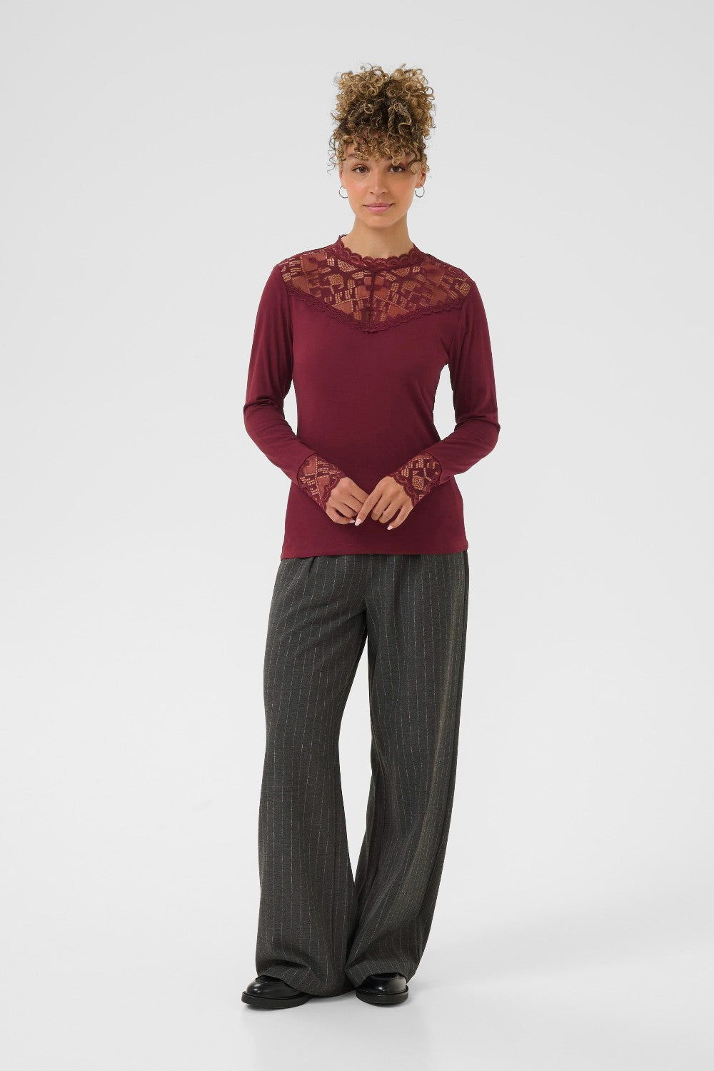 Person wearing a burgundy top with lace details and gray pants on a white background