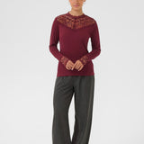 Person wearing a burgundy top with lace details and gray pants on a white background