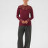 Person wearing a burgundy top with lace details and gray pants on a white background