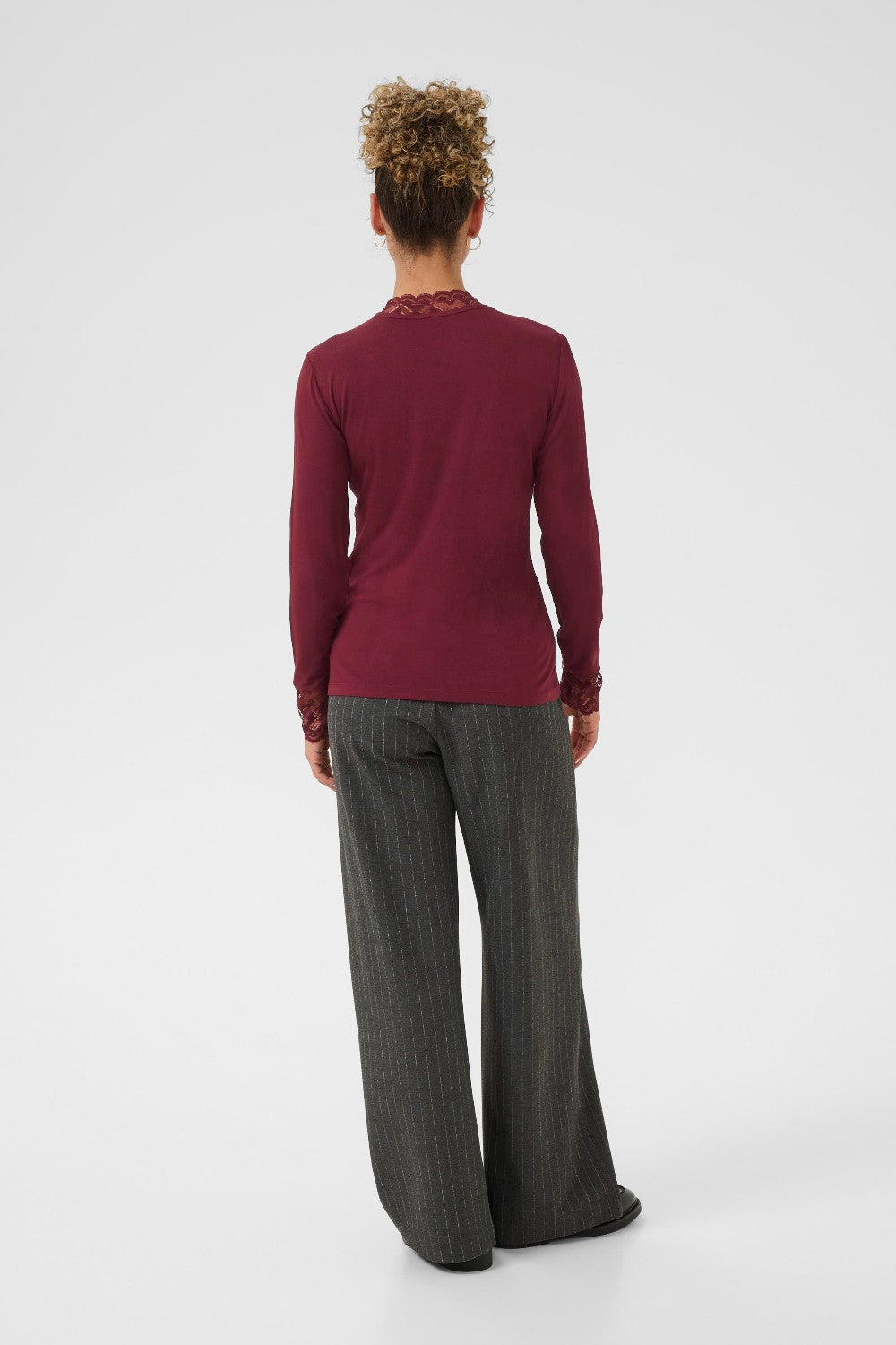 Person wearing a burgundy long-sleeve top and gray pants on a white background