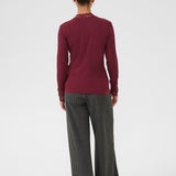 Person wearing a burgundy long-sleeve top and gray pants on a white background