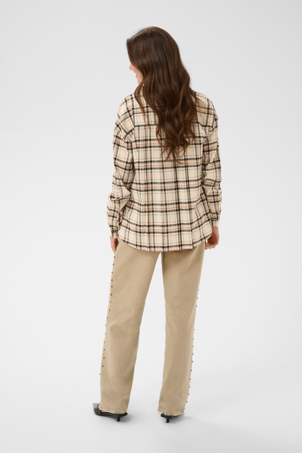 Woman wearing a plaid shirt and beige pants on a white background