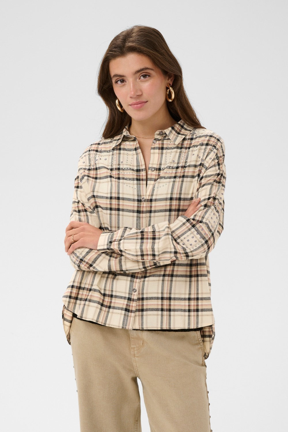 Woman wearing a plaid shirt and beige pants on a plain background