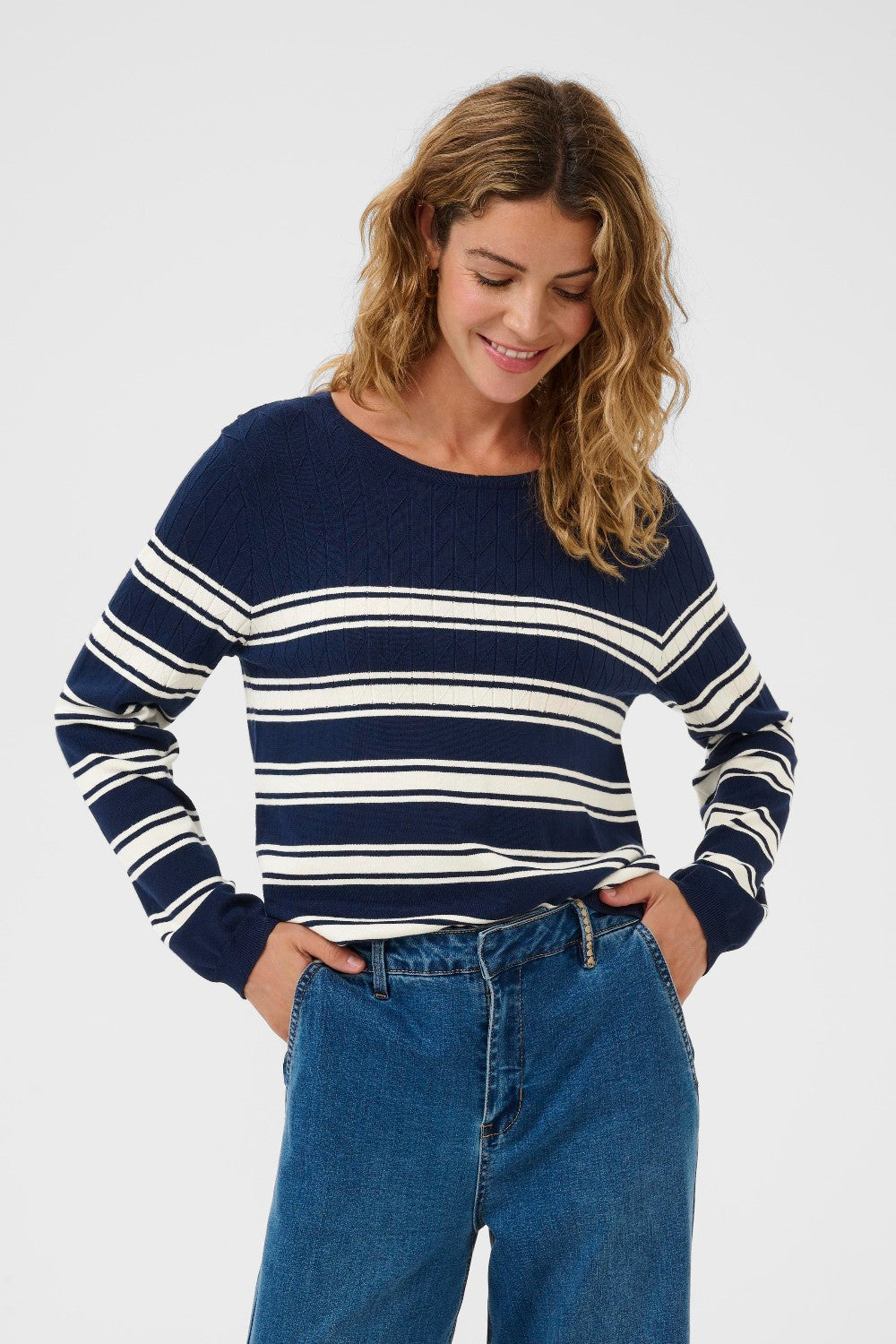 Woman wearing navy and white striped sweater with jeans on a white background