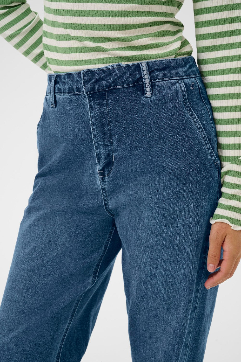 Person wearing blue jeans and a green and white striped shirt on a plain background