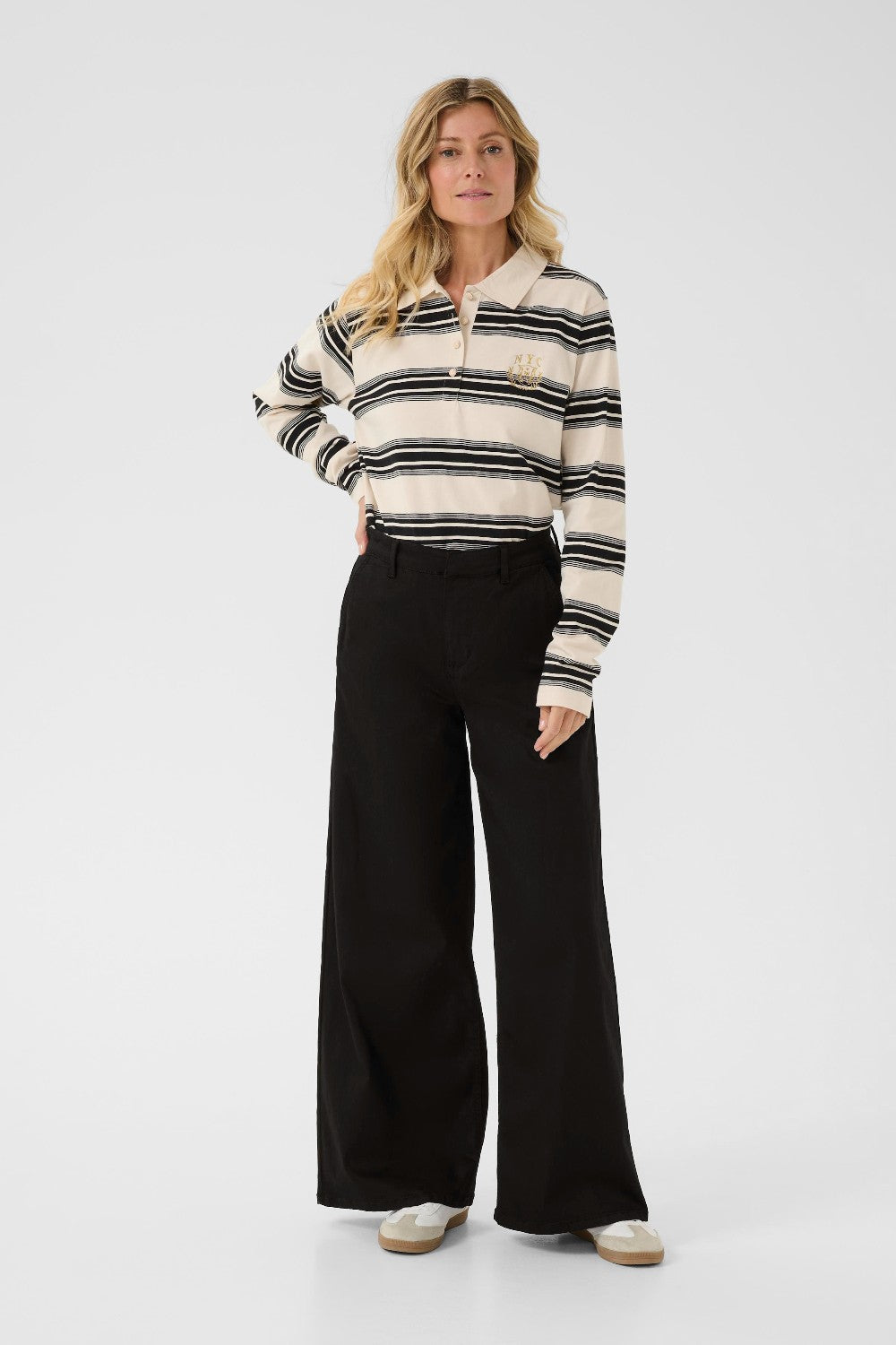 Woman wearing a black and white striped shirt with a collar and black wide-leg pants on a white background