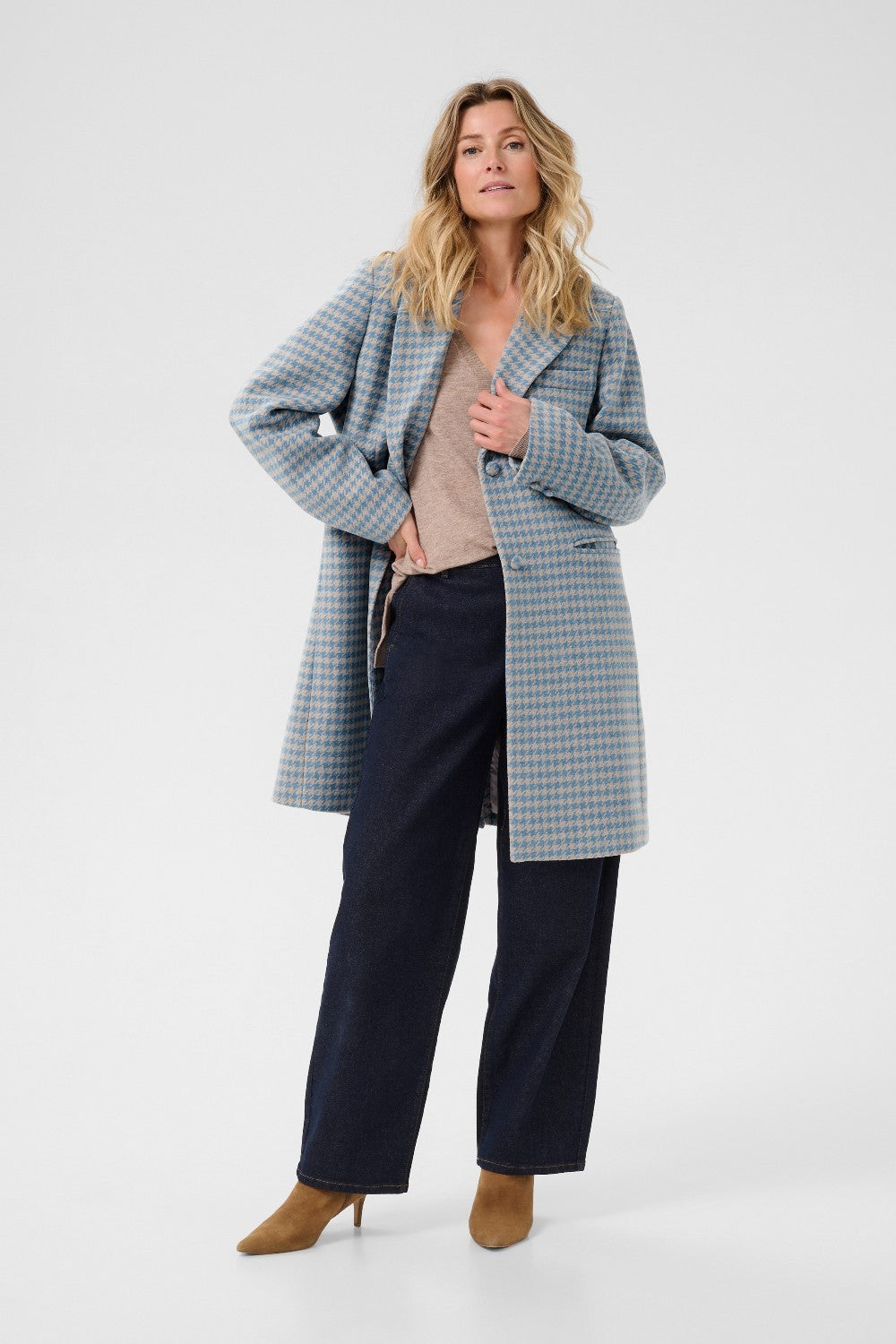 Woman wearing a checkered coat over a sweater and pants on a white background