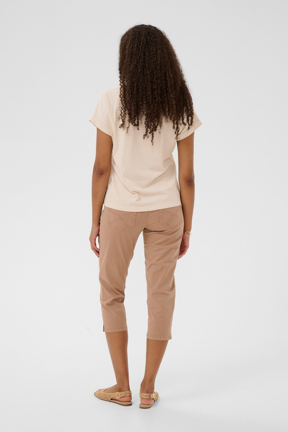 Person wearing a beige t-shirt and tan capri pants on a white background