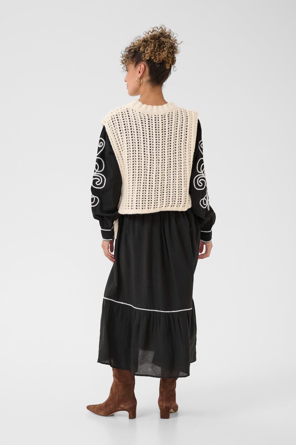 Person wearing a black dress with an off white crochet top on a white background